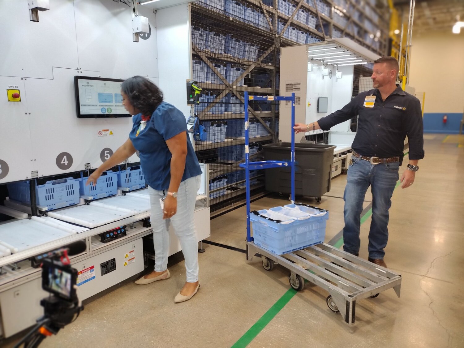 Walmart team lead Anna Mearidy (left) and store manager Robert Smith demonstrate how a customer order is fulfilled after robots bring the requested items to the Static Work Station at Walmart’s fulfillment center at 25108 Market Place Drive in Katy.